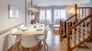 Een eetgedeelte met een houten tafel, witte stoelen, hanglampen en een trap met houten spijlen.