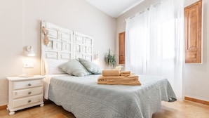 Een slaapkamer met een bed, nachtkastje, lamp en gordijnen.