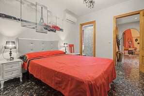 Une chambre à coucher avec un grand lit, une table de chevet, une lampe, un miroir et une porte donnant sur une autre pièce.