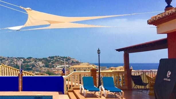 Un espace piscine avec des chaises longues, une vue sur la mer et un paysage urbain en arrière-plan.