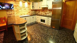 Une cuisine dotée d’un comptoir en granit, de meubles blancs, d’un réfrigérateur en acier inoxydable et d’un coin bar.