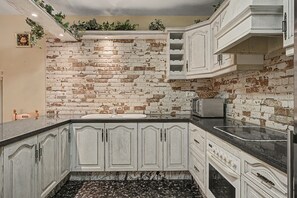 Een keuken met witte kasten, een bakstenen muur, een marmeren aanrechtblad en een inbouwoven.