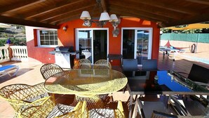 Une terrasse extérieure avec une table ronde, des chaises en osier, un barbecue et une piscine.