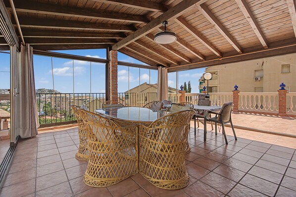 A covered outdoor dining area with wicker furniture and a view of the cityscape.