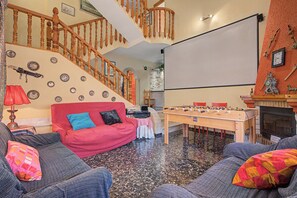 Een woonkamer met een rode bank, een houten trap, een tafelvoetbaltafel en een open haard.