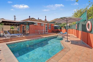 Une piscine avec des chaises longues et des parasols, un patio couvert et un bâtiment rouge avec un toit en tuiles.