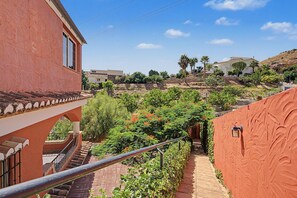 A residential area with terraced houses, a staircase leading to a balcony, and a view of a hillside with vegetation.