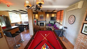 Une table de billard avec des billes, un coin bar, une cheminée et une horloge au mur.