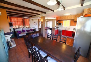 Un vaste espace de vie comprenant une grande table à manger en bois, des meubles de cuisine rouges et une cheminée en briques.