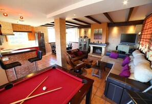 Une table de billard, un coin salon, une cheminée et un téléviseur dans le salon.
