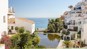 Un bâtiment situé sur la côte, offrant une vue sur la mer, avec un petit étang et une végétation luxuriante tout autour.