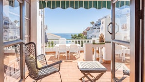 Un balcon avec vue sur la mer, des meubles blancs et un auvent vert.