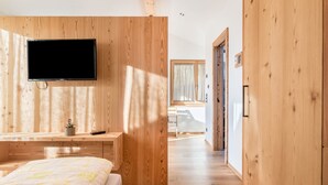 A modern bedroom with a wooden wall, a flat-screen TV, a bed with a patterned bedspread, and a desk with a plant. - Apartment "Guntschöllerhof Hochwart" with Mountain View, Wi-Fi, Balcony & Garden (Völs)