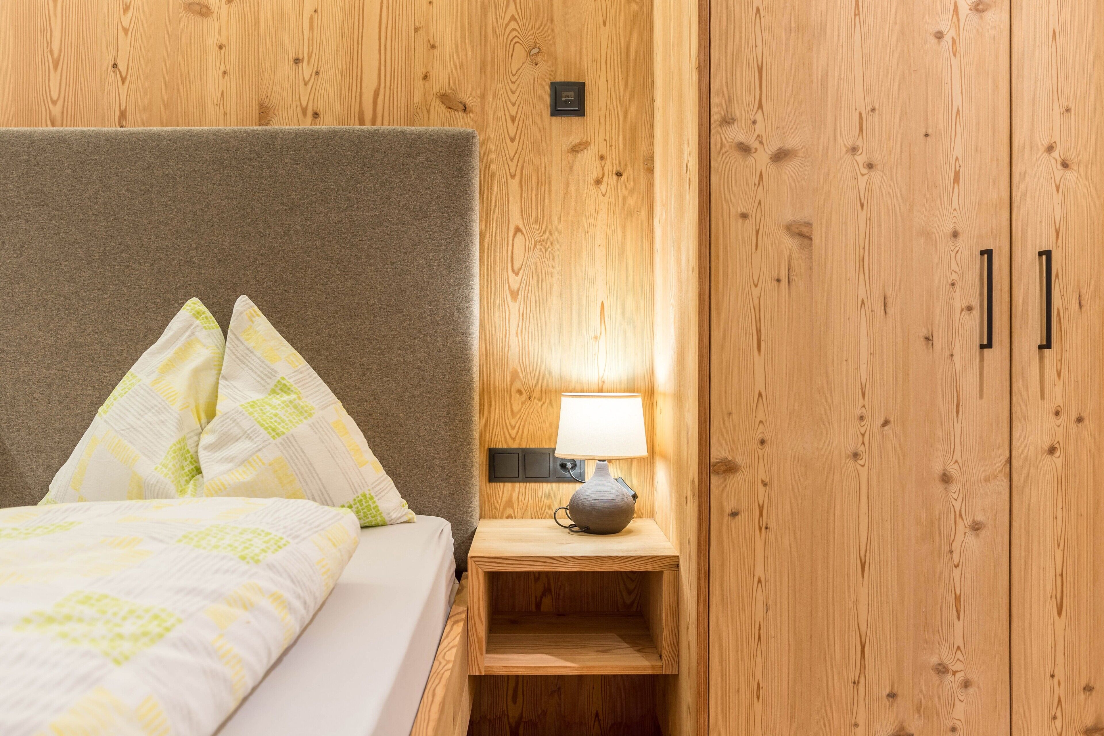 Una habitación con paneles de madera, una cama, una mesita de noche con lámpara y un armario.