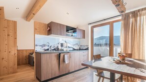 A modern kitchen with wooden cabinets, a large window, and a dining area with a table and chairs. - Apartment "Guntschöllerhof Hochwart" with Mountain View, Wi-Fi, Balcony & Garden (Völs)