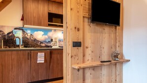 A wooden kitchen with a flat-screen TV, a coffee machine, and a shelf with a jar. - Apartment "Guntschöllerhof Völseggspitze" with Mountain View, Wi-Fi, Balcony & Garden (Völs)