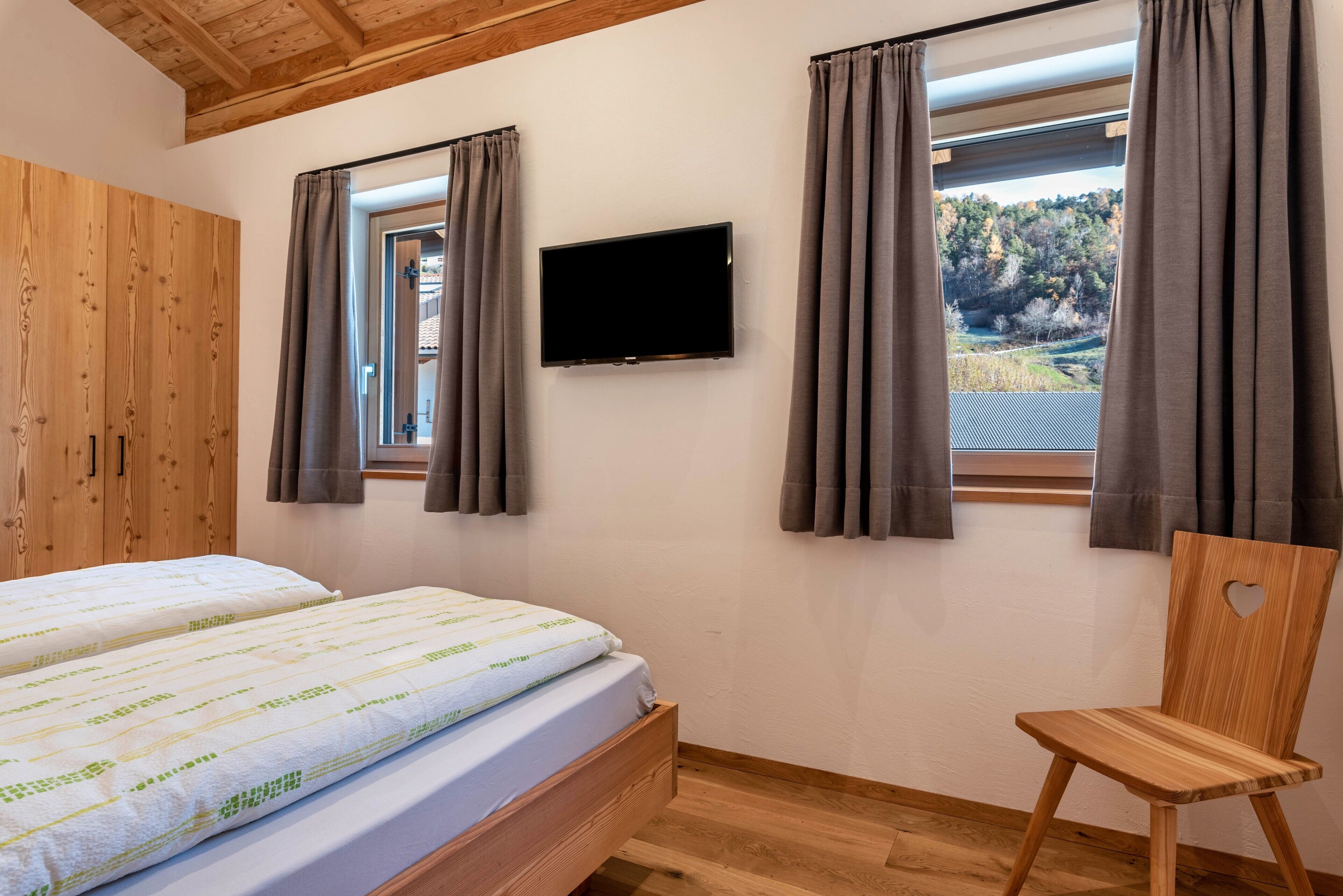 Een slaapkamer met een bed, een televisie, een houten kledingkast en een stoel.