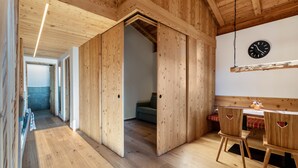 A wooden interior with a dining area, a clock on the wall, and a hallway leading to another room. - Apartment "Guntschöllerhof Völseggspitze" with Mountain View, Wi-Fi, Balcony & Garden (Völs)
