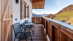 Une terrasse en bois avec une table et des chaises, une rambarde en bois et une vue sur un paysage montagneux.
