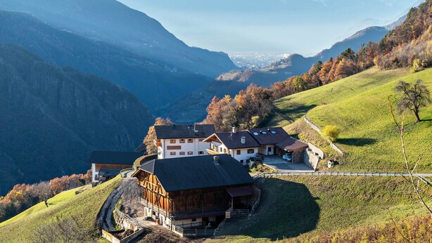 A mountain lodge with a large wooden building, a smaller attached structure, and a view of a valley and mountains.