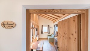 A wooden interior with a dining area, a sofa, and a kitchen visible through an open door.