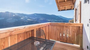 A wooden balcony with a table and chair, overlooking a mountainous landscape.