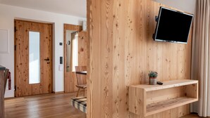Ein modernes Zimmer mit Holzwandverkleidung, einem Wand-Fernseher, einem kleinen Regal und einer Tür mit Milchglasfenster.