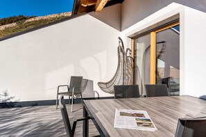 Une terrasse extérieure avec une table en bois, des chaises et un fauteuil en osier.
