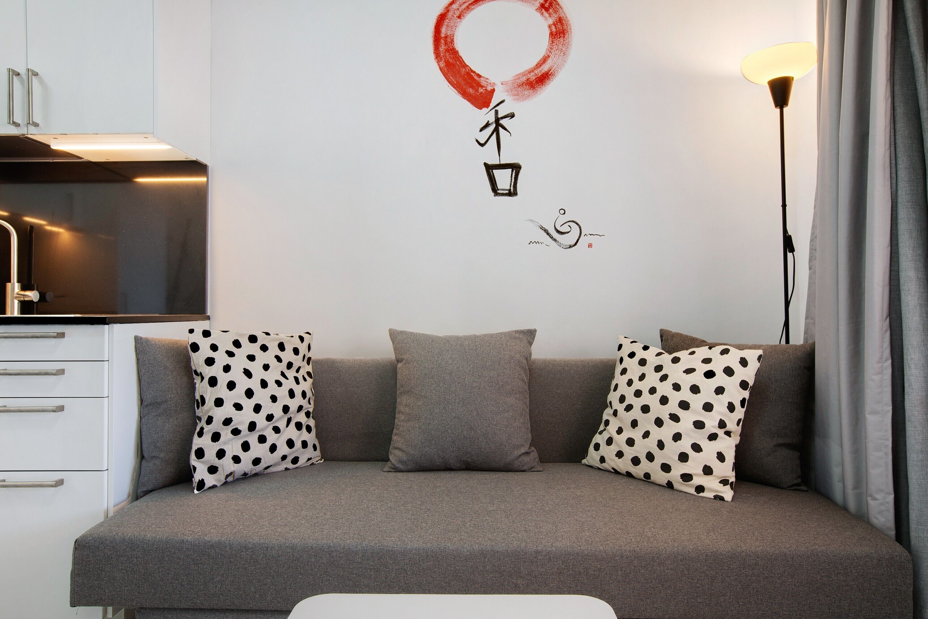 A modern living space with a sofa, pillows, a wall with Chinese characters, a lamp, and a kitchen area.