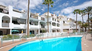 A swimming pool with a white fence, palm trees, and a multi-story building with balconies. - Apartment "Casa Princesa" with Sea & Mountain View, Pool, Balcony & Wi-Fi (Playa del Cura)