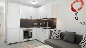 A modern kitchen with white cabinets, a built-in oven, and a grey sofa with patterned cushions. - Apartment "Casa Princesa" with Sea & Mountain View, Pool, Balcony & Wi-Fi (Playa del Cura)