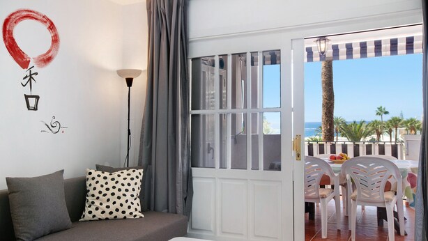 A room with a sofa, a small table, a window with curtains, and a view of the outdoors. - Apartment "Casa Princesa" with Sea & Mountain View, Pool, Balcony & Wi-Fi (Playa del Cura)