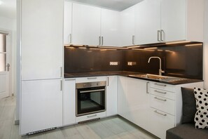 Una cocina moderna con armarios blancos, una encimera negra, un fregadero de acero inoxidable y un horno.