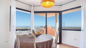 Un balcón con una mesa preparada para dos, una silla de mimbre y vista al mar.