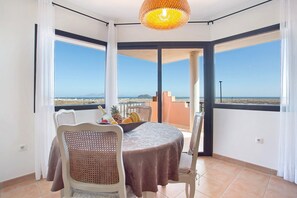 Un balcon avec une table dressée pour deux personnes, une chaise en osier et une vue sur la mer.