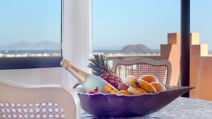 Una mesa con una cesta de frutas que incluye piña, plátanos y naranjas, y una botella de champán.
