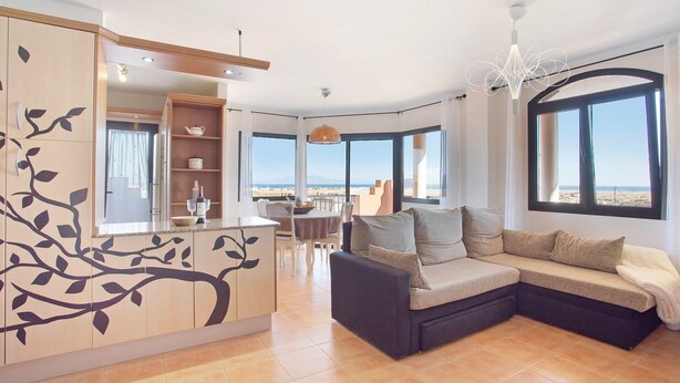 Una sala de estar moderna con un sofá seccional, una zona de comedor con mesa y sillas, y grandes ventanales con vistas.