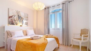 Un dormitorio con cama, una silla, un cuadro y una ventana.