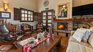Ein gemütliches Wohnzimmer mit Kamin, Holzmöbeln, Fernseher und einer Wanduhr.