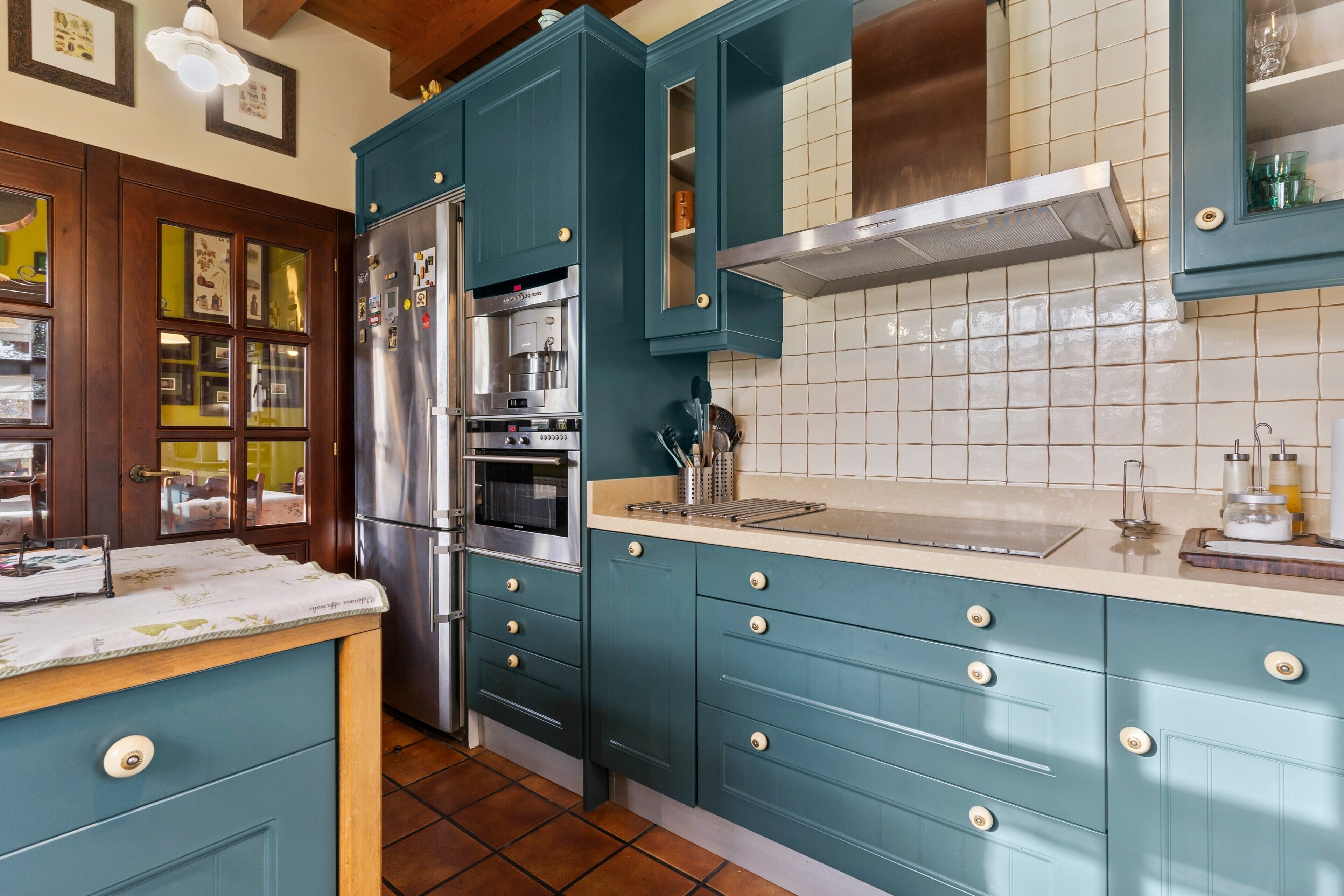 Una cocina con armarios color turquesa, un refrigerador de acero inoxidable y un salpicadero de azulejos.