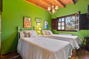 Une chambre avec deux lits, un plafond en bois, une fenêtre avec des volets et des œuvres d’art mural.