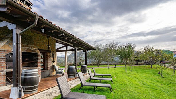 Eine Terrasse mit Sitzgelegenheit und ein Steinhaus mit Schornstein.