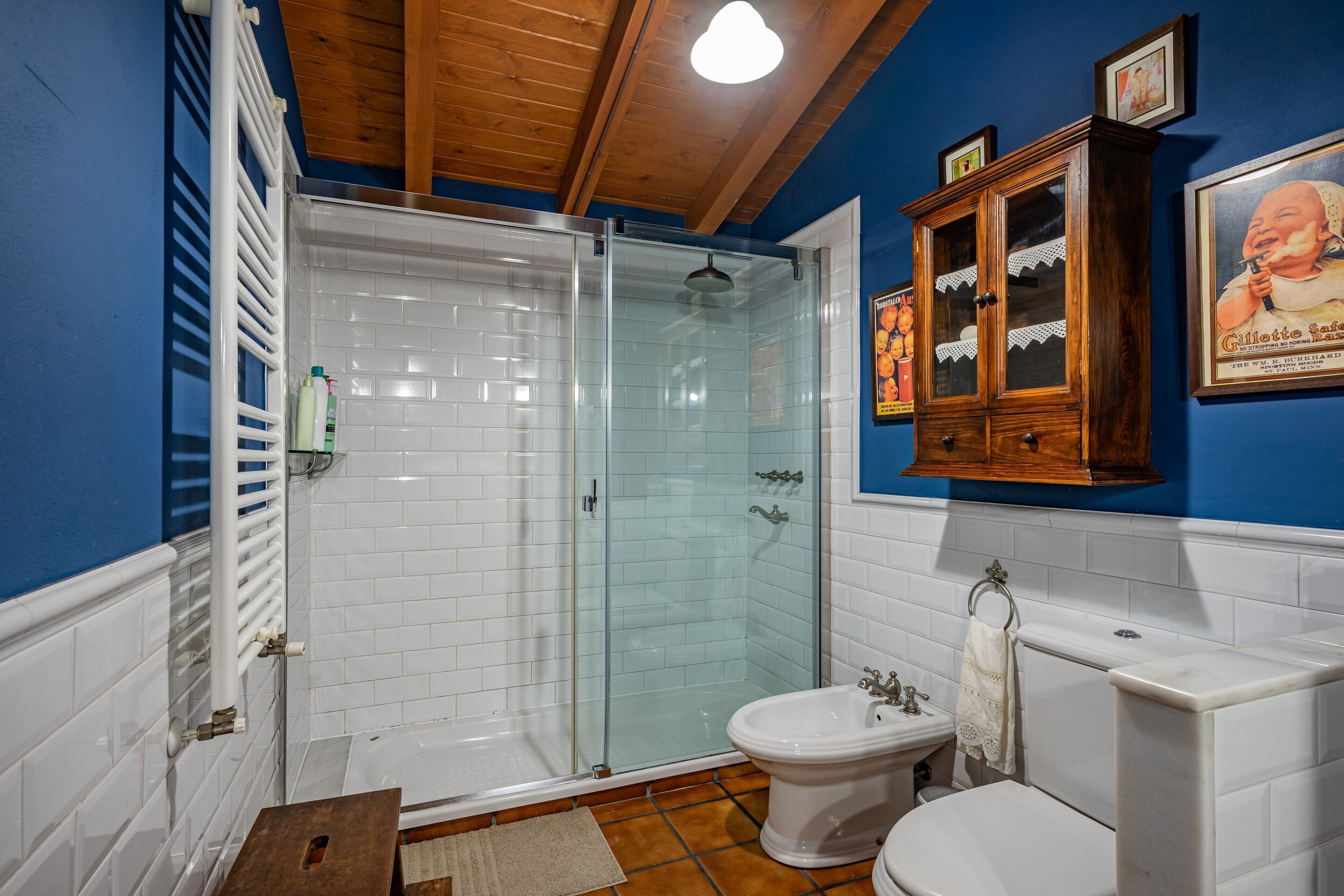 Un baño con mampara de vidrio, inodoro blanco, bidé y mueble de madera.