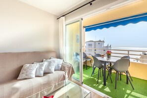 Un balcón con mesa y sillas, un sofá con cojines y vista al mar.