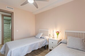 Een slaapkamer met twee bedden, een nachtkastje, een plafondventilator en een raam met jaloezieën.