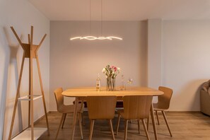 Een eetgedeelte met een houten tafel, stoelen, een vaas met bloemen, een fles en een glas.