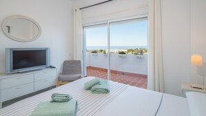 A hotel room with a bed, a television, a chair, a balcony with a view, and a lamp. - Spacious and Fantastic Views Apartment with Sea View, Pool, Garden & Wi-Fi (Nueva Andalucía)