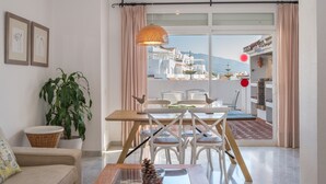 A dining area with a wooden table, white chairs, and a hanging light fixture. - Spacious and Fantastic Views Apartment with Sea View, Pool, Garden & Wi-Fi (Nueva Andalucía)