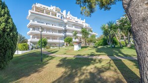 A multi-story residential building with balconies, surrounded by well-maintained grass and trees. - Spacious and Fantastic Views Apartment with Sea View, Pool, Garden & Wi-Fi (Nueva Andalucía)