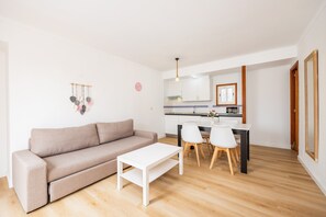 Un salon moderne avec un canapé, une table blanche et un coin cuisine comprenant une table à manger et des chaises.